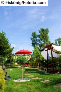 Das Bild zeigt einen Garten mit einem roten Sonnenschirm in der Mitte (Eiskönig / Fotolia.com).